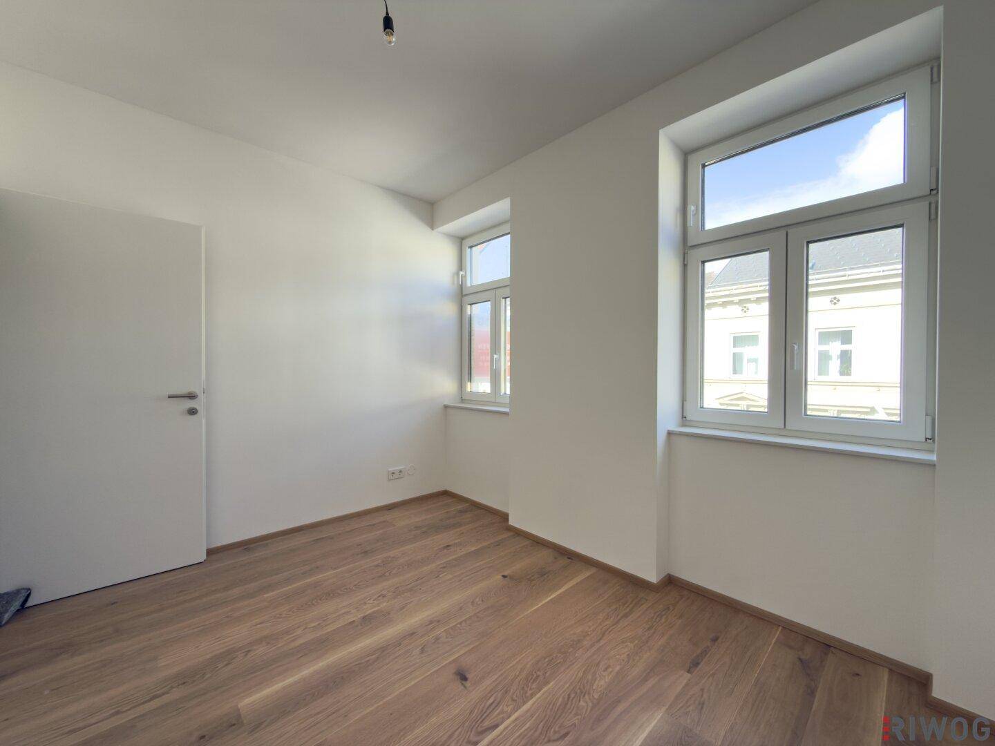 Freundliches Zimmer mit zwei großen Fenstern und neu verlegtem Parkettboden, ideal für individuelle Gestaltung.