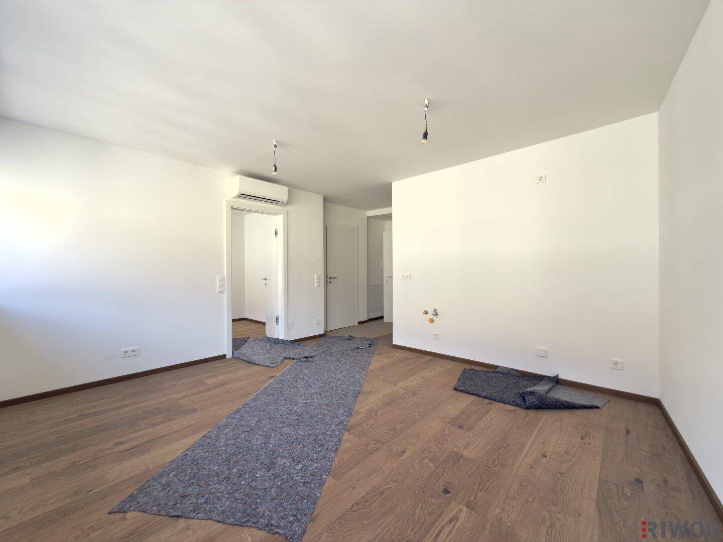 Geräumiges Zimmer mit Holzboden, weißen Wänden und Zugang zu weiteren Räumen.