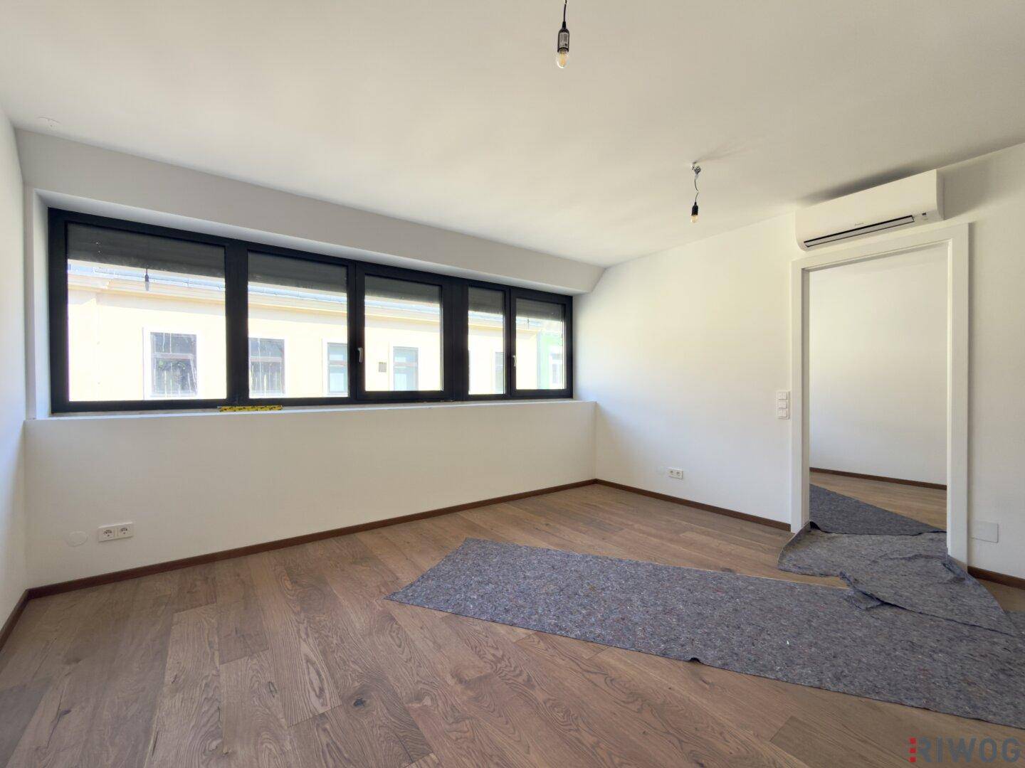 Helles Zimmer mit Holzboden, großen Fenstern und Klimaanlage in neuwertigem Zustand.