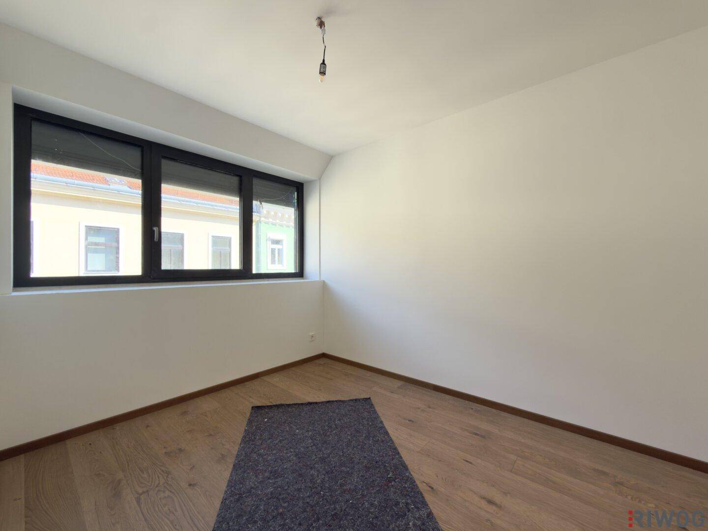 Heller Raum mit breiten Fenstern, Holzboden und sauberer, weißer Gestaltung.