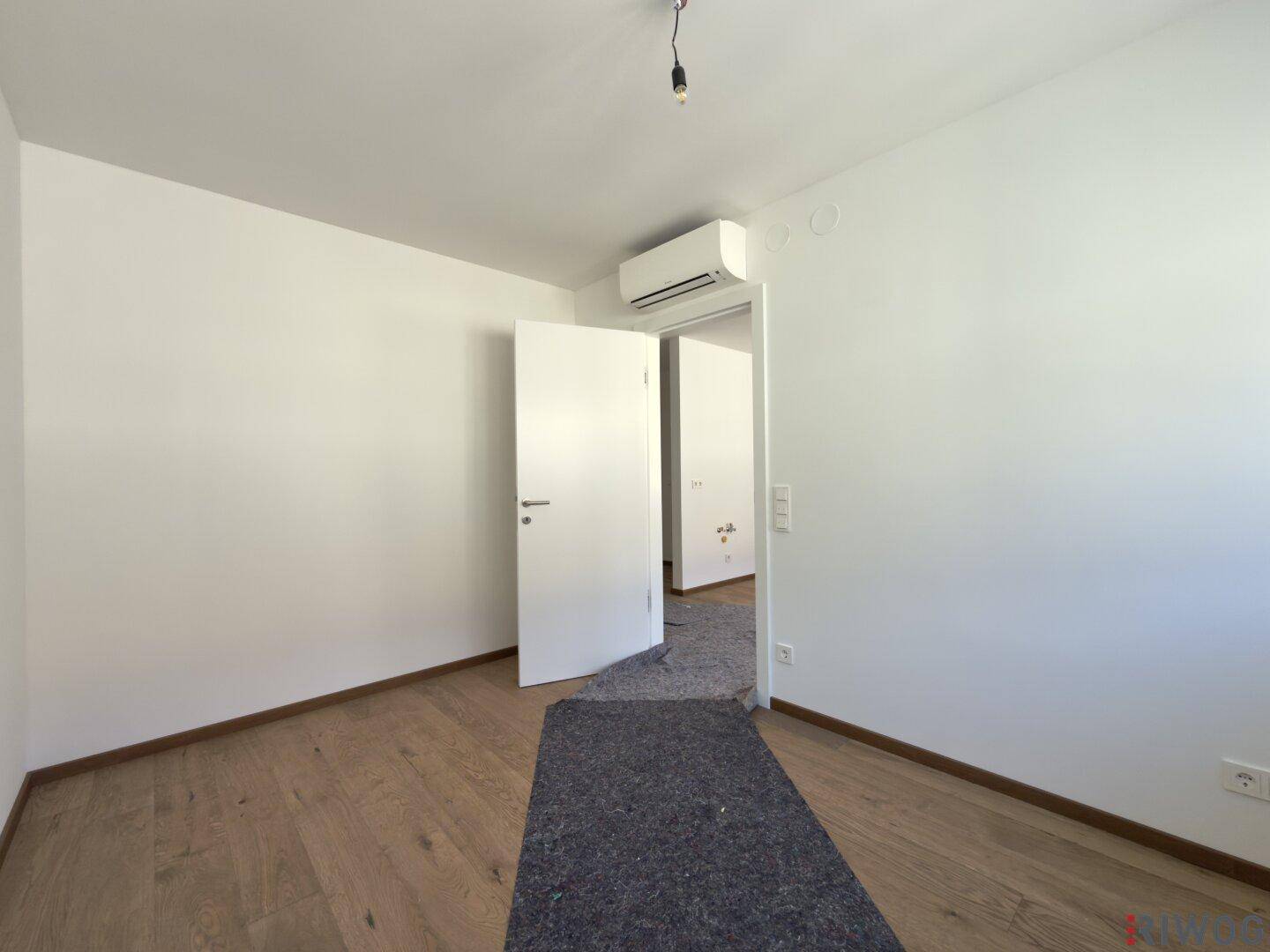Geräumiges Zimmer mit Klimaanlage, Holzboden und Zugang zu weiteren Räumen.
