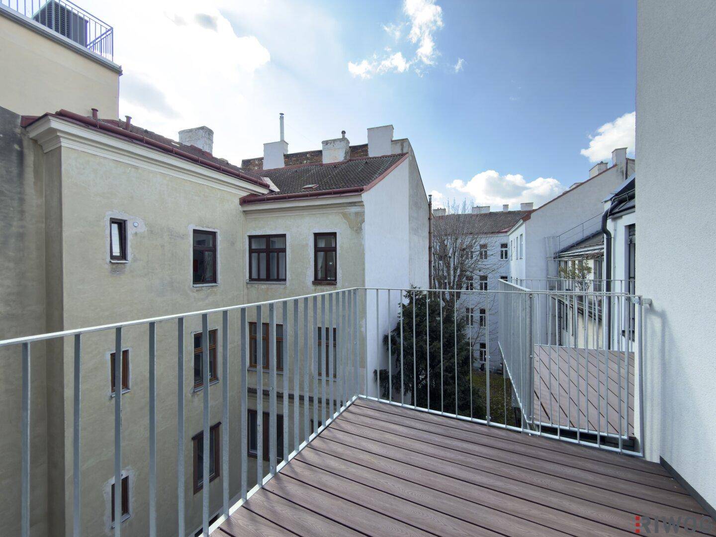 Geräumiger Balkon mit Holzboden und Metallgeländer, bietet einen Blick auf den Innenhof und umliegende Gebäude.