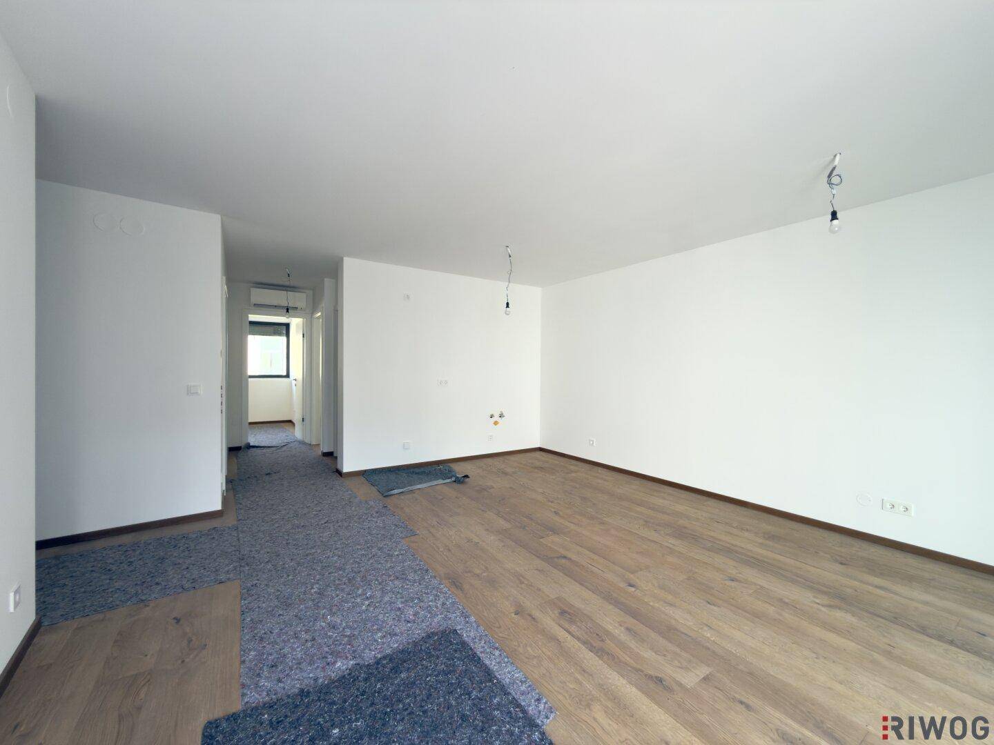 Offener Wohnbereich mit Holzboden, der in einen Flur übergeht und weitere Räume erschließt.