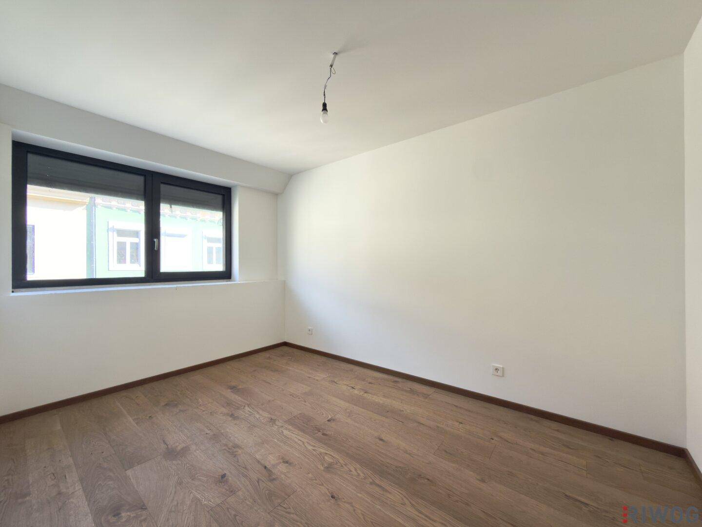 Helles Schlafzimmer mit Holzboden und einem großen Fenster mit Blick auf die Umgebung.