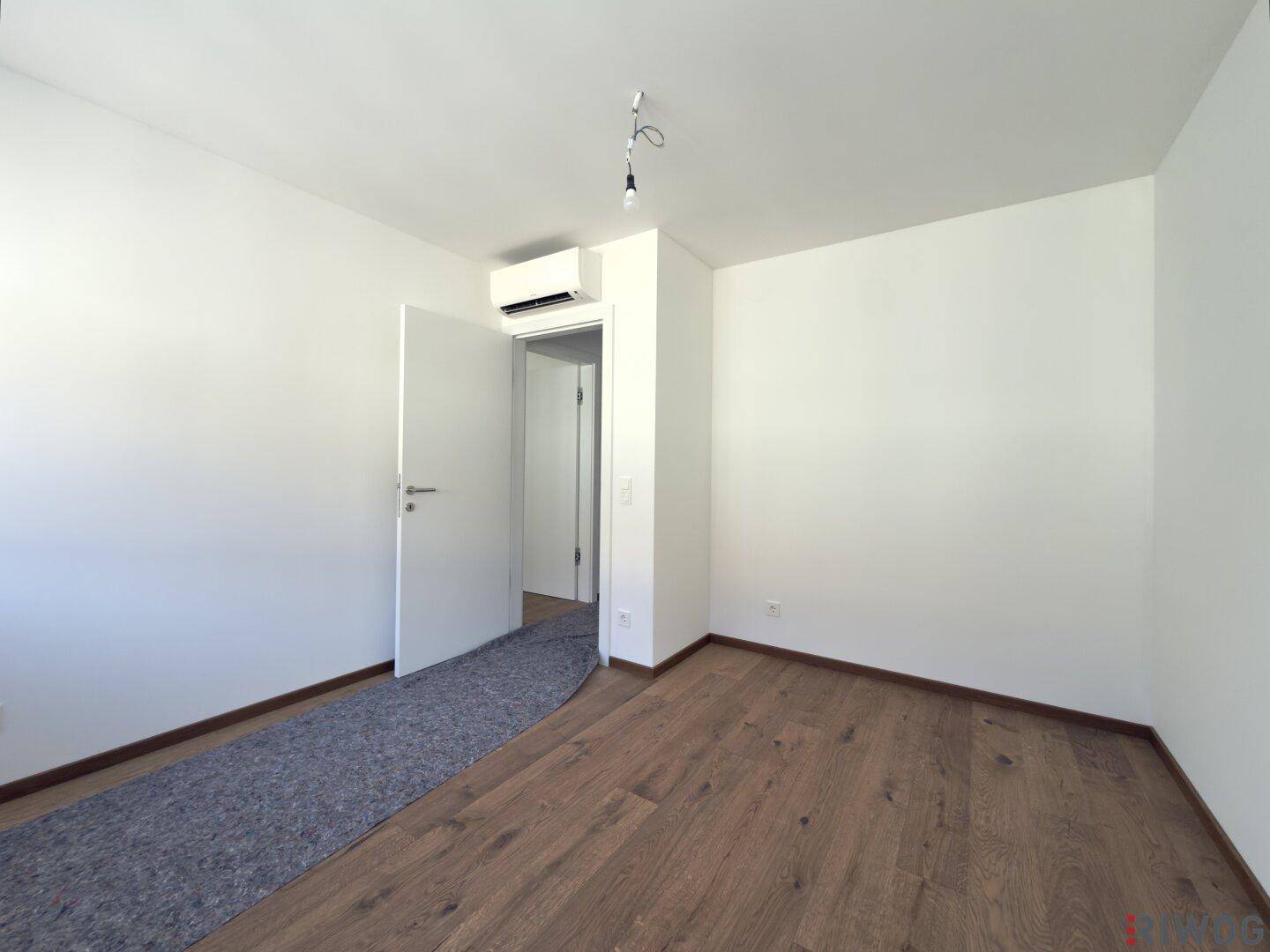 Schlafzimmer mit Holzboden, weiß gestrichenen Wänden und Klimaanlage über der Tür.