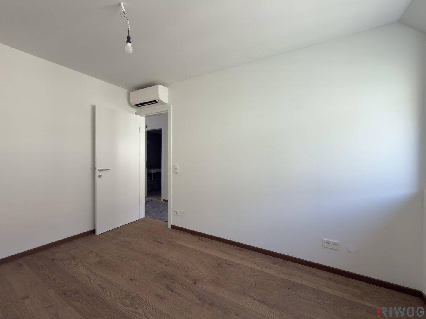 Schlafzimmer mit Holzboden, weiß gestrichenen Wänden und einer Klimaanlage an der Wand.