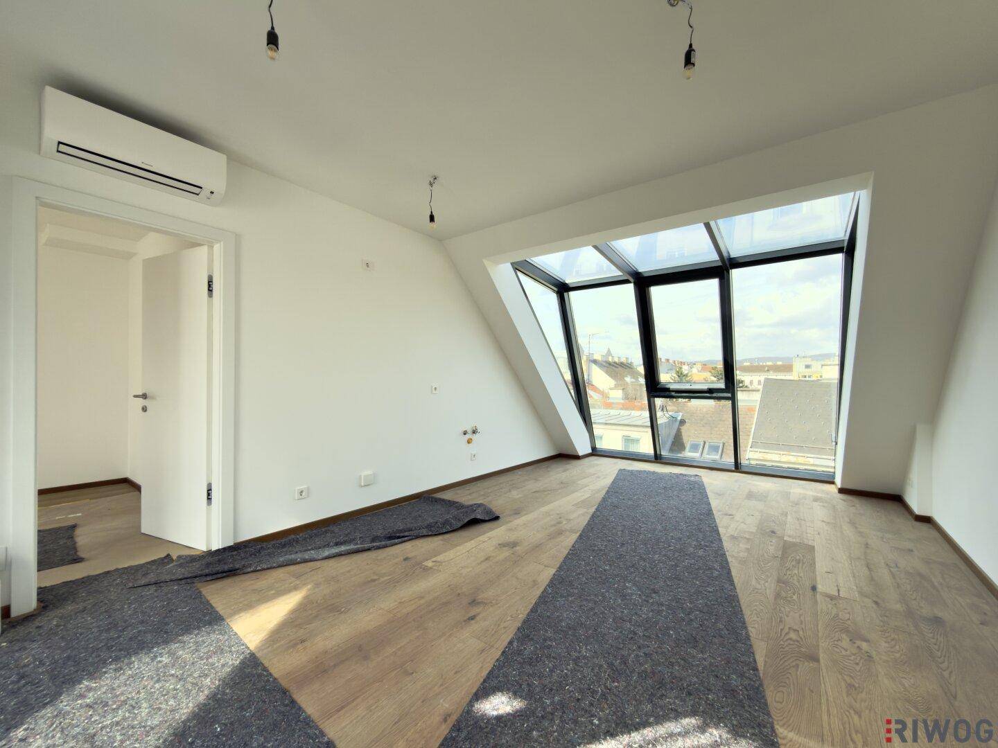Heller Raum mit Klimaanlage, schrägen Fenstern und Holzboden, bietet moderne Wohnqualität und Ausblick.
