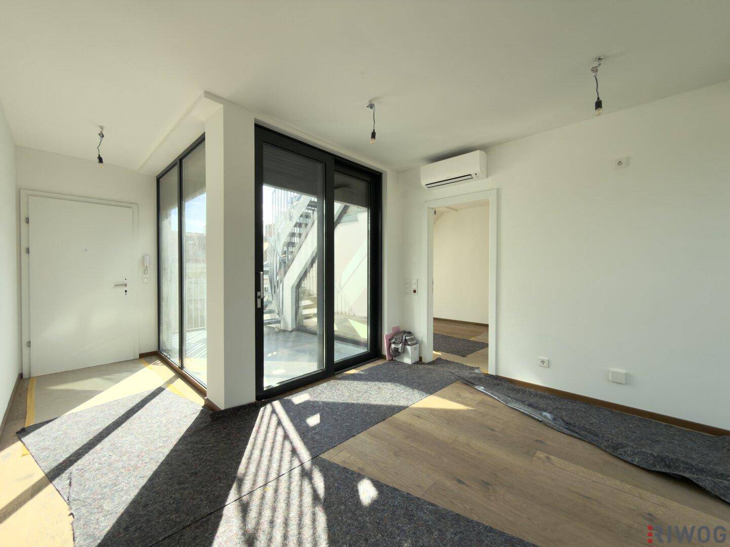 Eingangsbereich mit großen Glasschiebetüren und Zugang zu einem sonnigen Außenbereich mit Treppe.