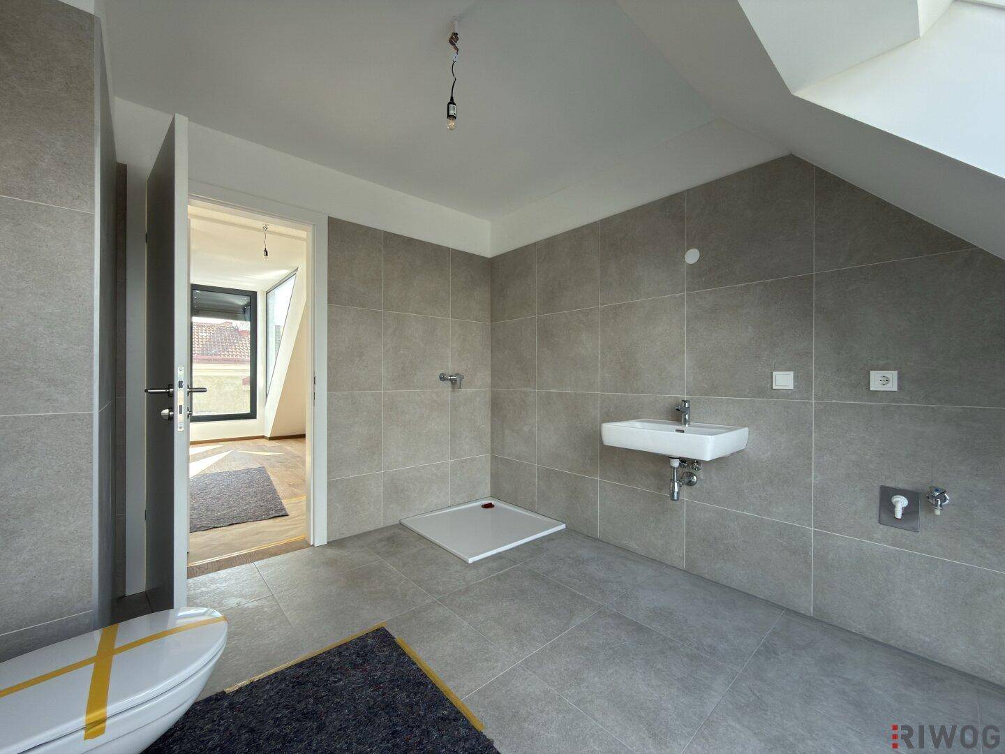 Modernes Badezimmer mit grauen Fliesen, wandhängendem Waschbecken und bodengleichem Duschbereich.