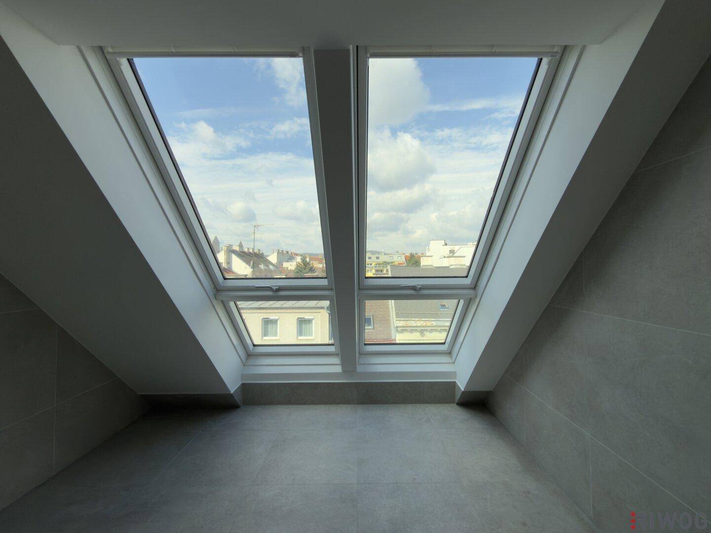 Helles Badezimmer mit Dachfenstern und Blick über die Stadt, ausgestattet mit grauen Fliesen.