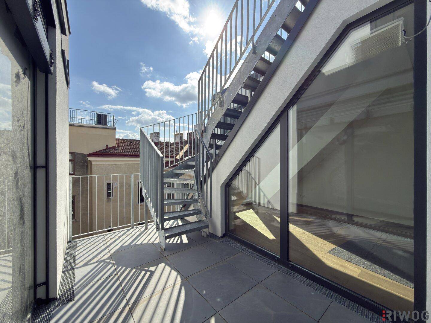 Sonnige Terrasse mit Metalltreppe, die zu einer weiteren Ebene führt, und Stadtblick.