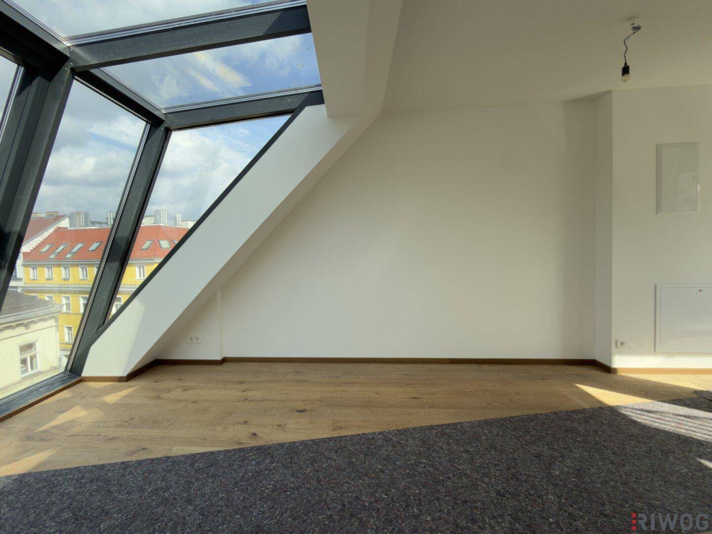 Geräumiger Raum mit beeindruckenden Schrägfenstern und Holzboden, bietet viel Tageslicht und Ausblick.