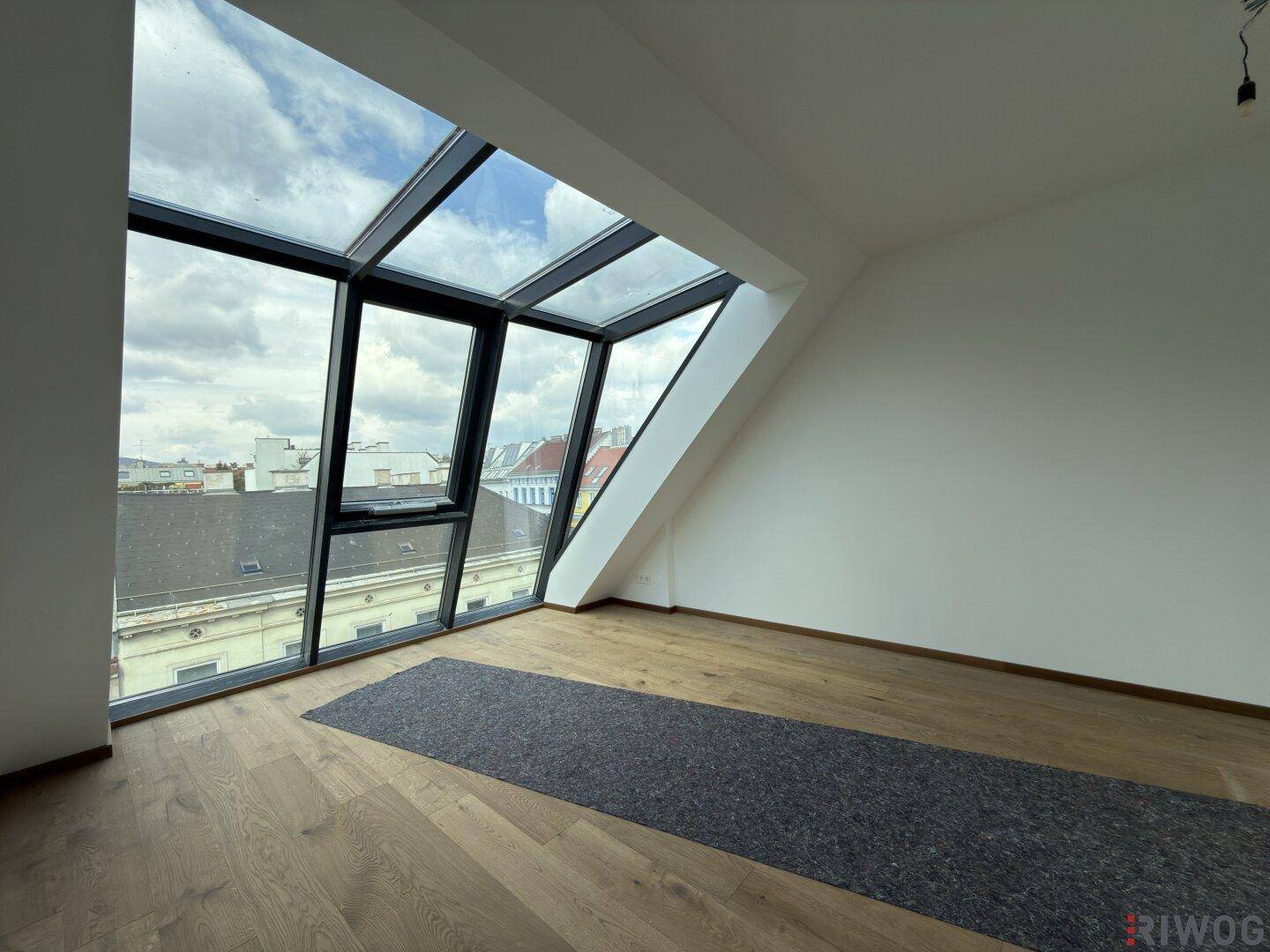 Lichtdurchfluteter Raum mit schrägen Glasfronten und Holzboden, ideal für individuelle Gestaltung.