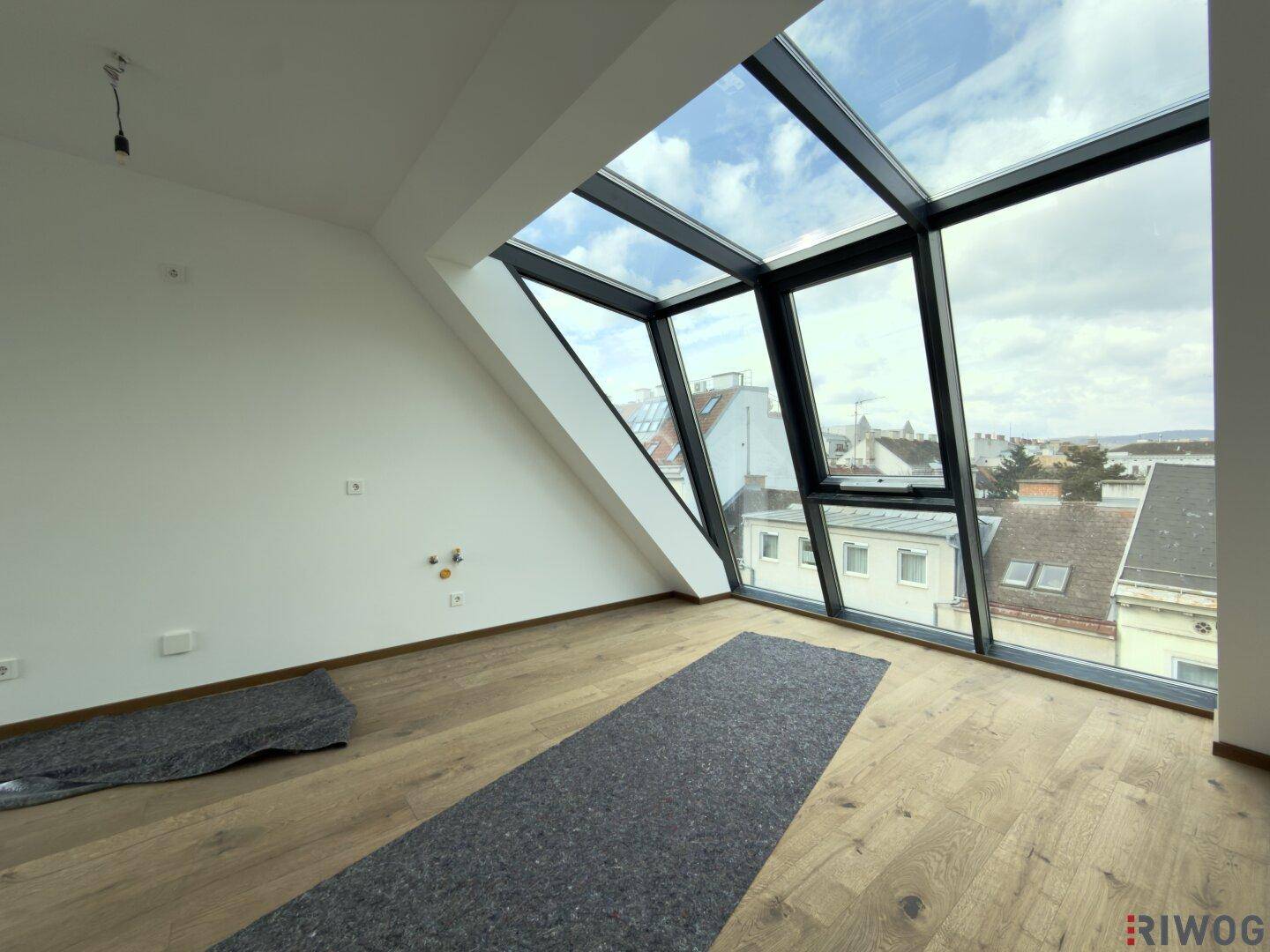 Heller, unmöblierter Raum mit großen, schrägen Glasfronten und Holzboden, bietet weite Aussicht.