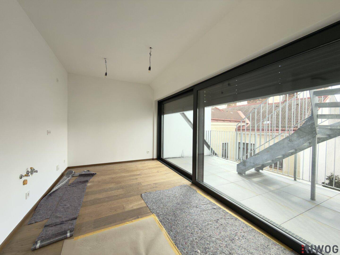 Heller Innenraum im Rohbau mit großen Schiebetüren und Zugang zu einer Außenterrasse.