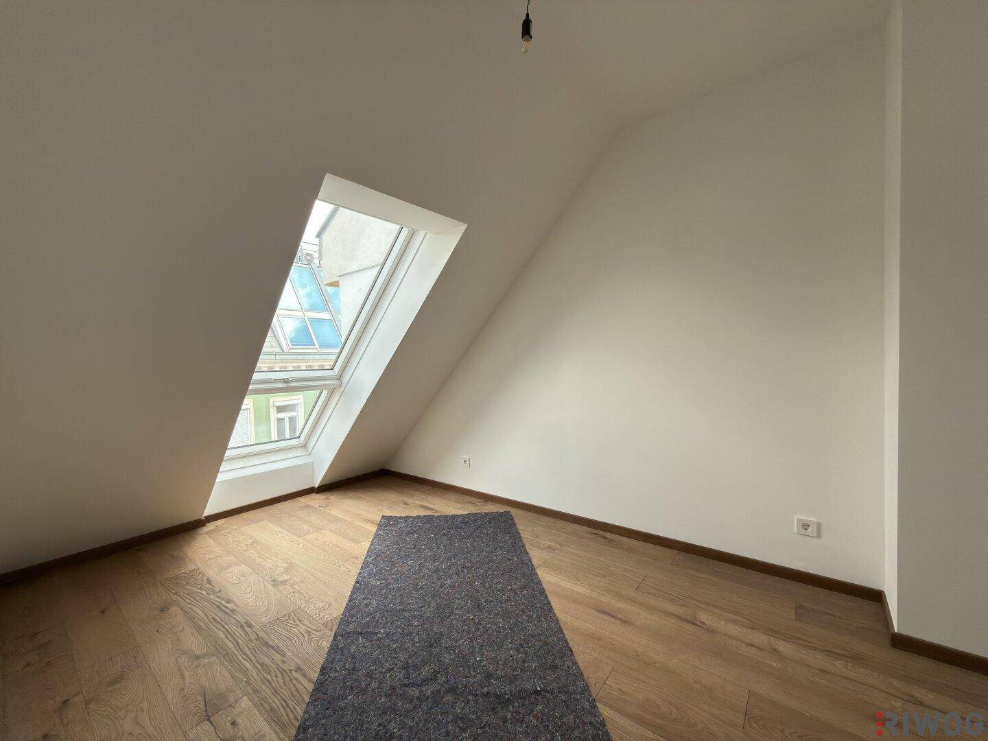 Dachgeschossraum mit Holzboden und großem Dachfenster, das viel Tageslicht hereinlässt.