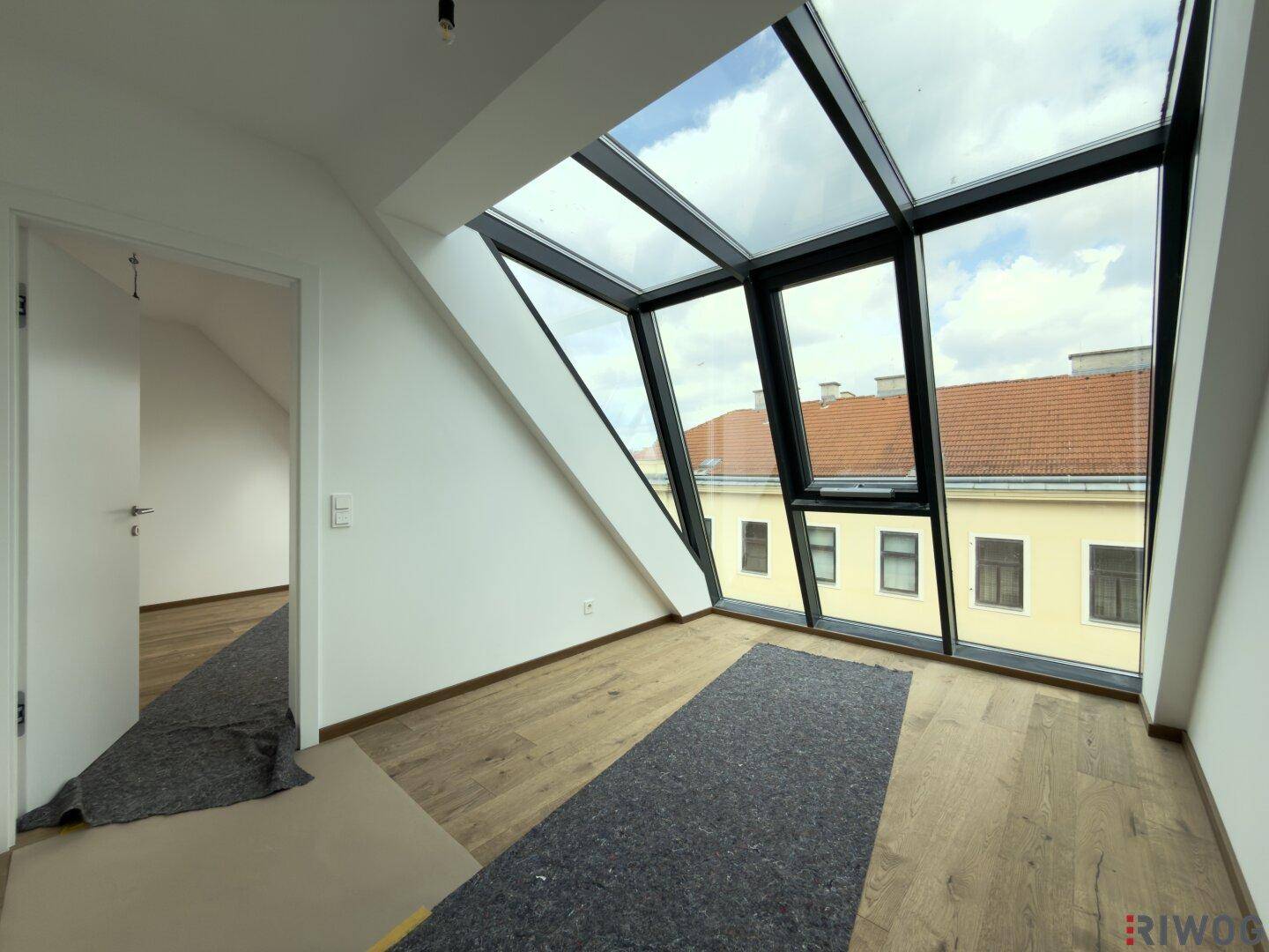 Lichtdurchfluteter Raum im Dachgeschoss mit großen Schrägfenstern und Holzboden.
