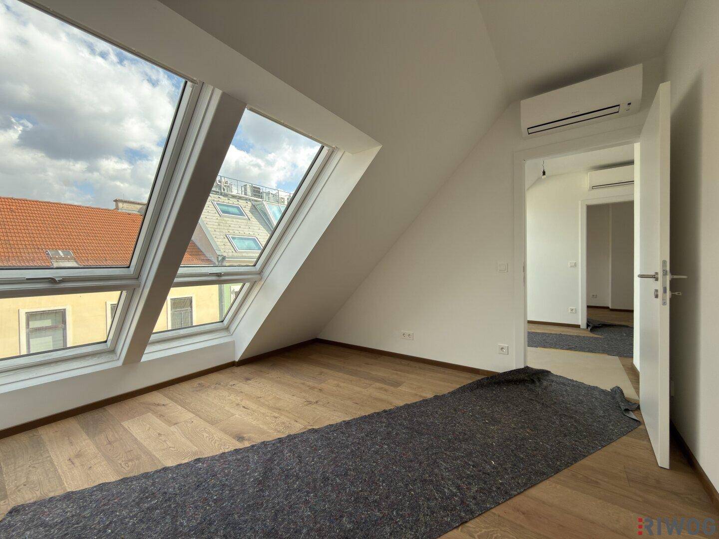 Heller Dachgeschossraum mit mehreren Dachfenstern und Holzboden, noch im Ausbau.