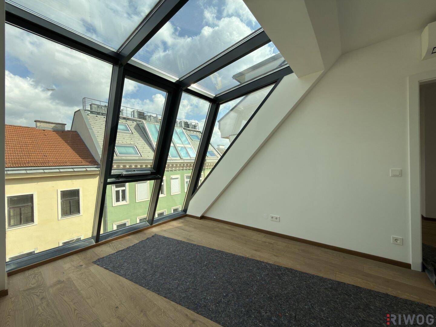Geräumiger Dachgeschossraum mit großen Schrägfenstern und Blick auf die umliegenden Dächer.