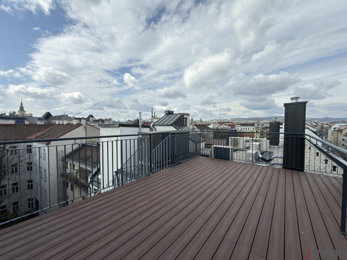 Geräumige Dachterrasse mit Holzboden und weitem Blick über die Stadt unter bewölktem Himmel.
