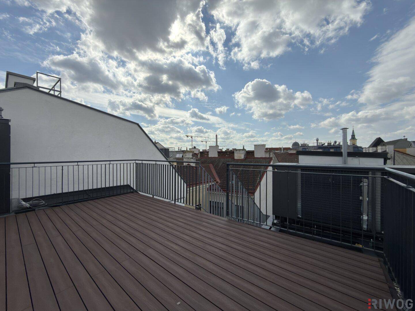 Weitläufige Dachterrasse mit Holzboden und Blick über die Dächer der Stadt unter bewölktem Himmel.