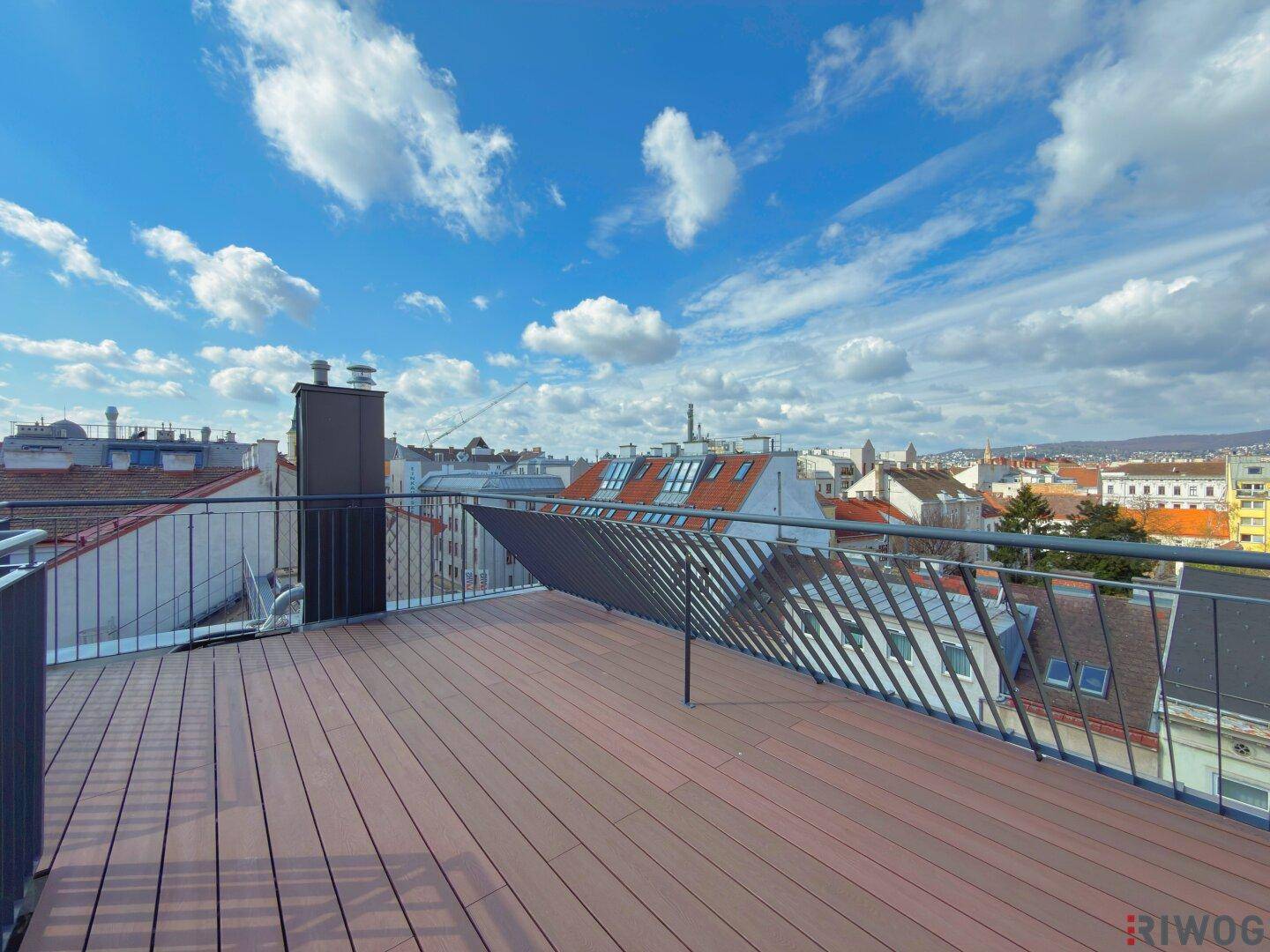 Weitläufige Dachterrasse mit Holzboden und Panoramablick über die Dächer der Stadt.