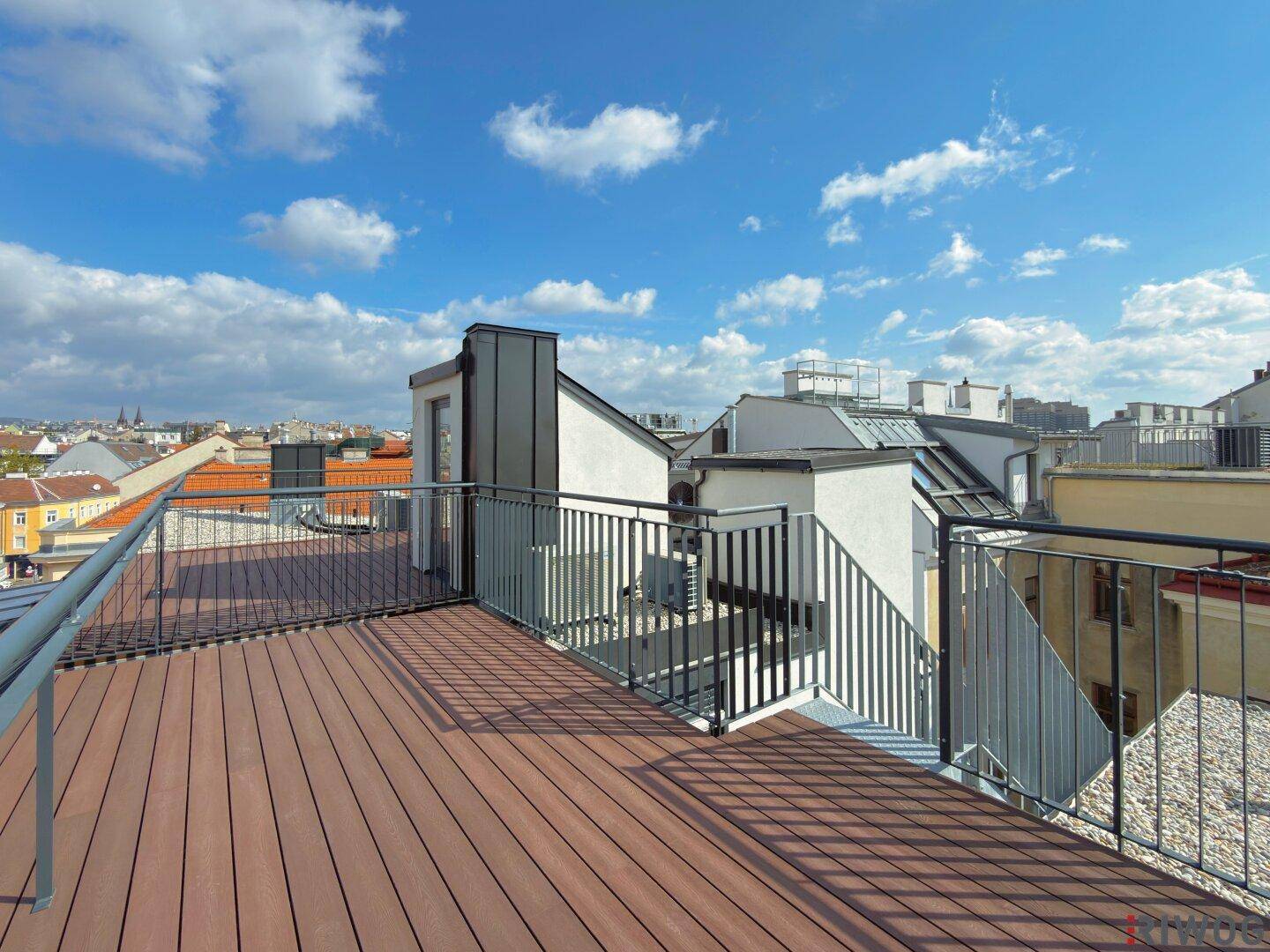 Geräumige Dachterrasse mit Holzboden und weitem Blick über die Stadt unter blauem Himmel.