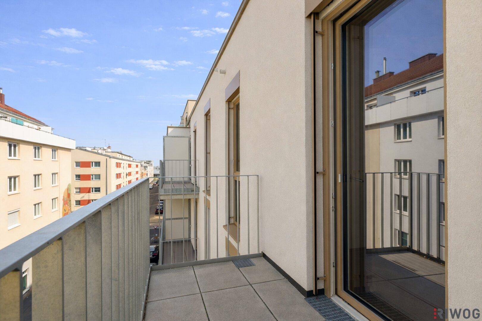 Langer Balkon mit Fliesenboden und Blick auf die moderne Architektur der Nachbargebäude.