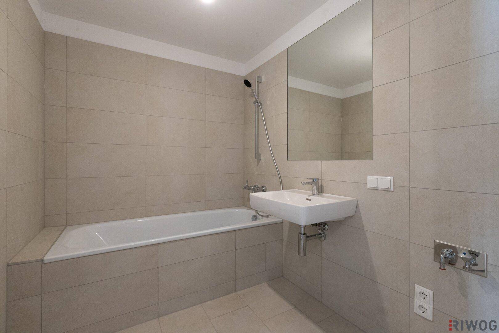 Sauberes Badezimmer mit Badewanne, modernem Waschbecken und hellen Wand- und Bodenfliesen.