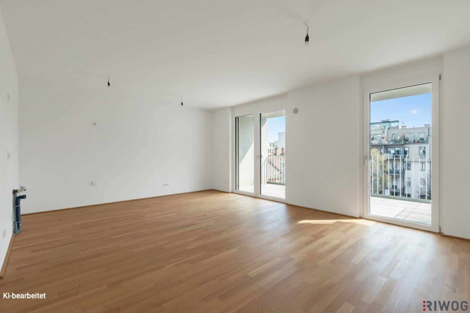 Helles, leeres Zimmer mit Parkettboden und Zugang zu zwei Balkonen.