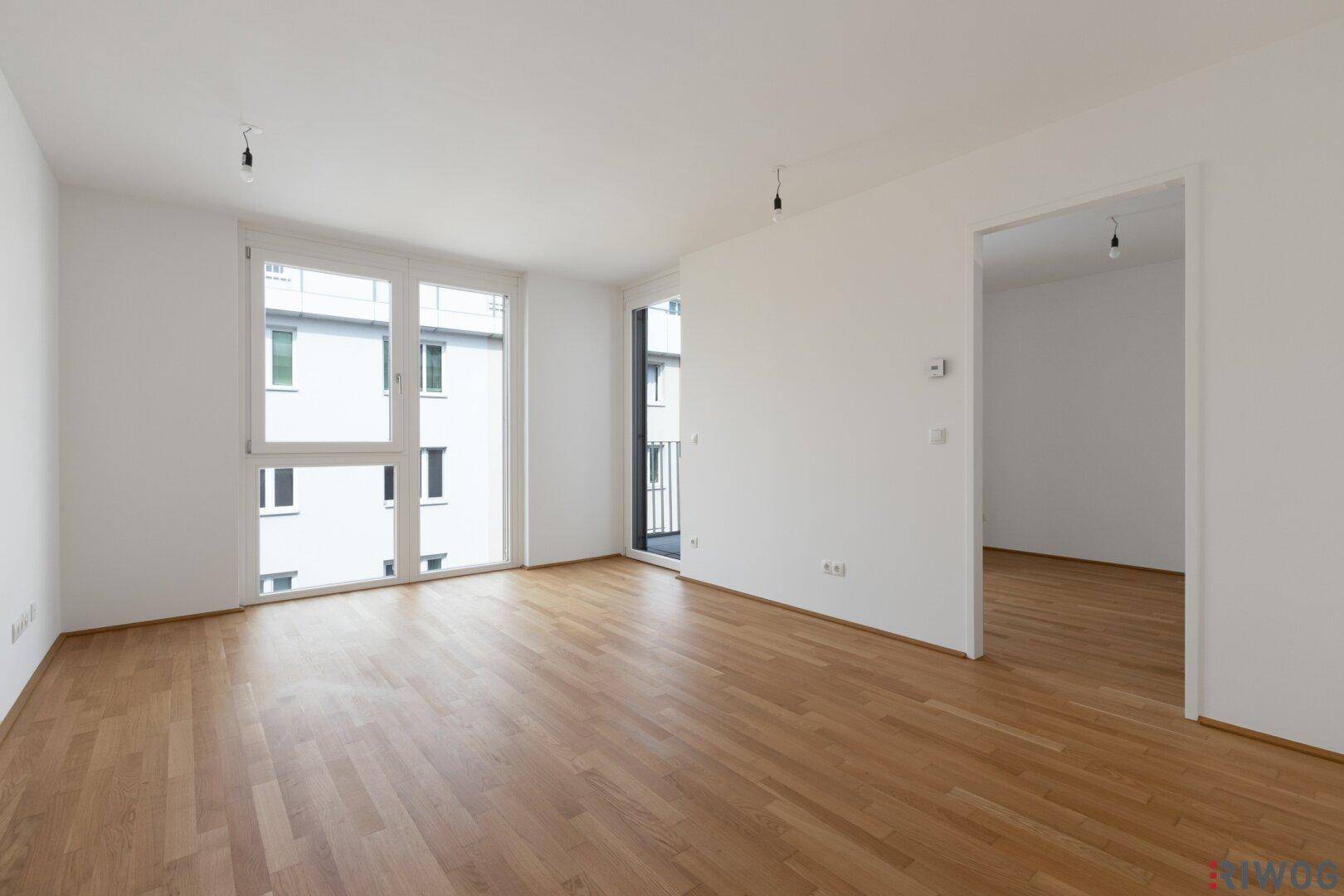 Geräumiges Wohnzimmer mit hellem Parkettboden und Zugang zum Balkon.