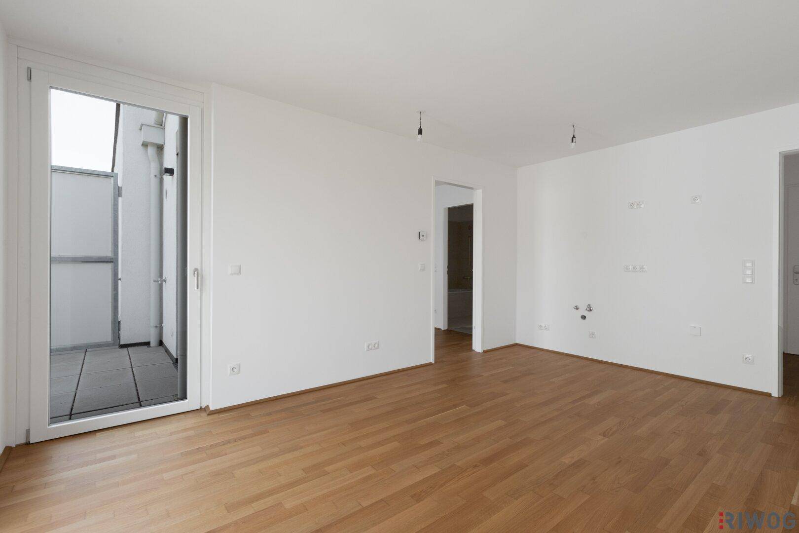 Helles Wohnzimmer mit Parkettboden und breiter Tür zum Außenbereich.