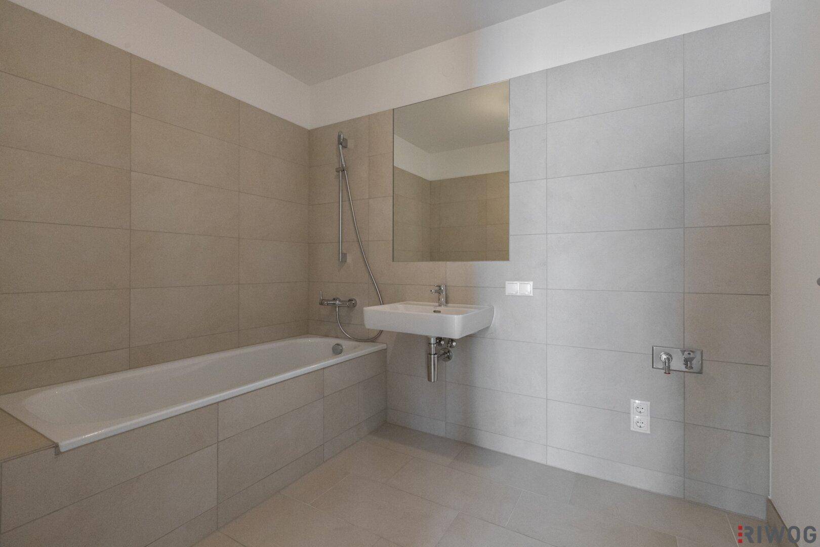 Modernes Badezimmer mit Badewanne, Waschbecken und großen Fliesen.