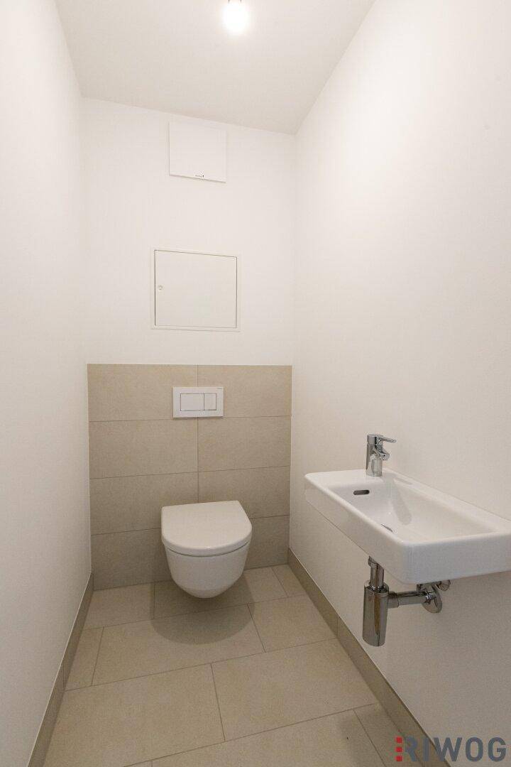 Gäste-WC mit wandhängender Toilette, kleinem Waschbecken und modernen Fliesen.