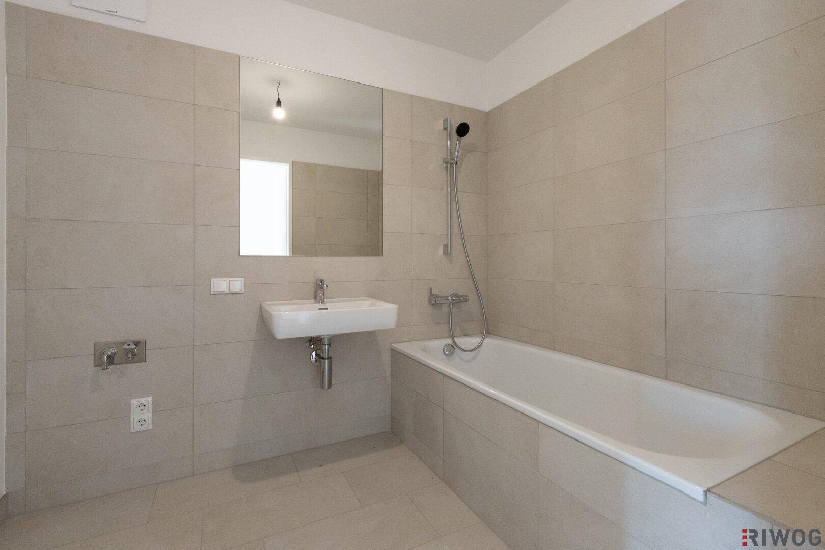 Modernes Badezimmer mit Badewanne, Wandwaschbecken und großen hellen Fliesen.