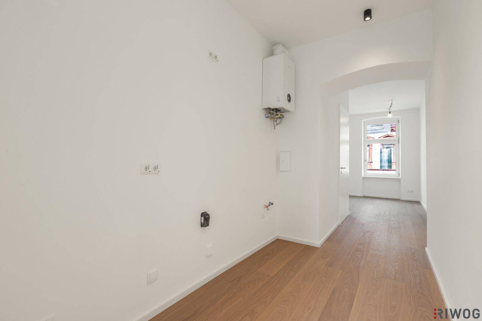 Funktionaler Raum mit Holzboden, weiß gestrichenen Wänden und einem Warmwasserbereiter an der Wand.