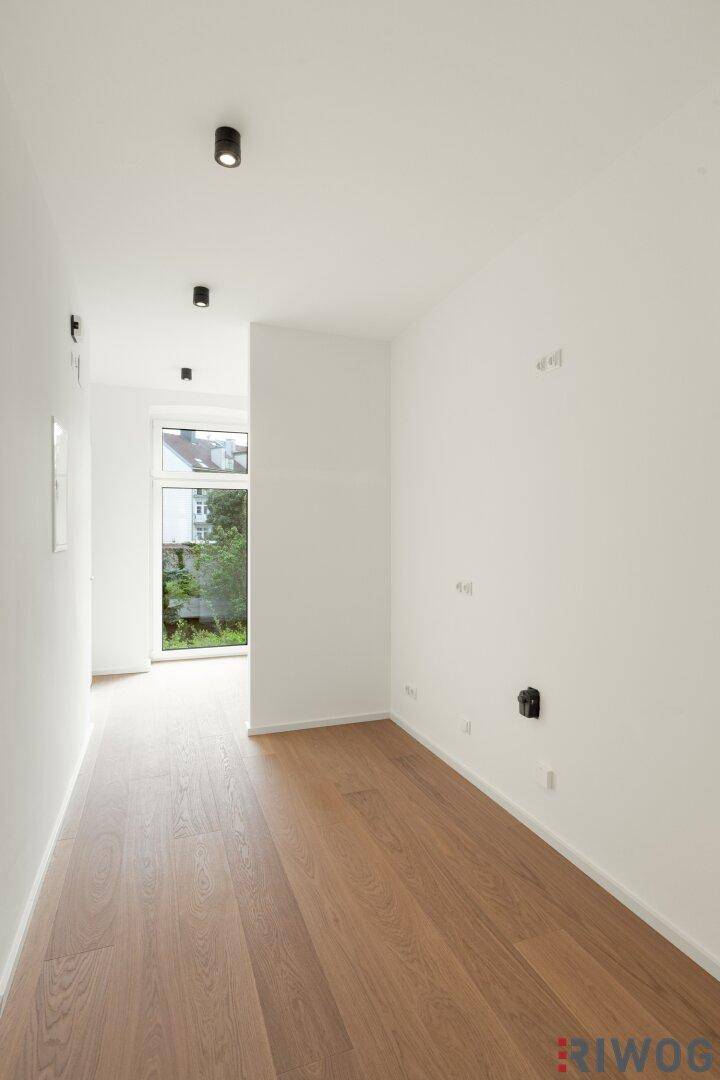 Heller Flur mit Holzboden und einem hohen Fenster am Ende, das Tageslicht hereinlässt.