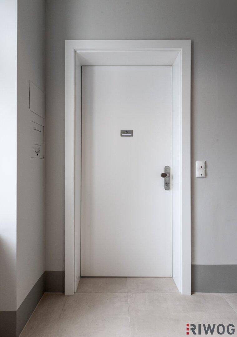 Weiße Innentür in einem hellen Flur mit grauen Wänden und modernem Lichtschalter.