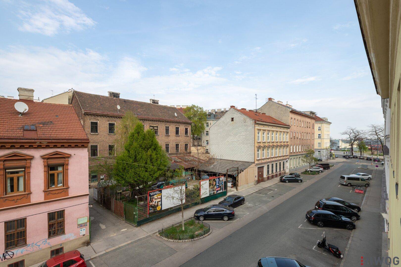 Weitläufiger Blick über eine städtische Straße mit parkenden Autos und umliegenden Gebäuden.