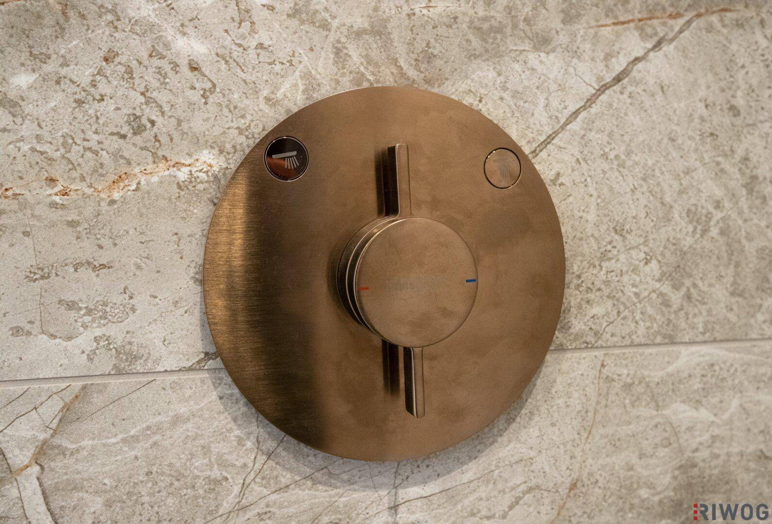 Detailansicht einer modernen Duscharmatur in gebürsteter Bronze-Optik an einer gefliesten Wand.