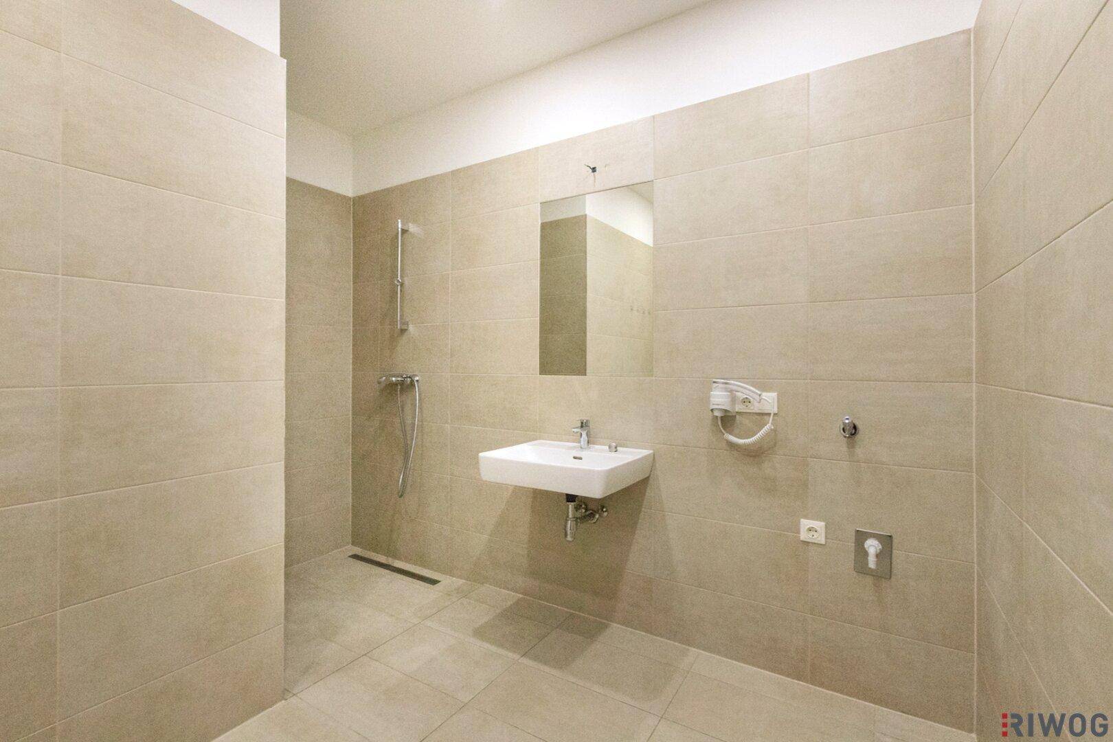 Modernes Badezimmer mit beigefarbenen Fliesen, ebenerdiger Dusche und wandmontiertem Waschbecken.