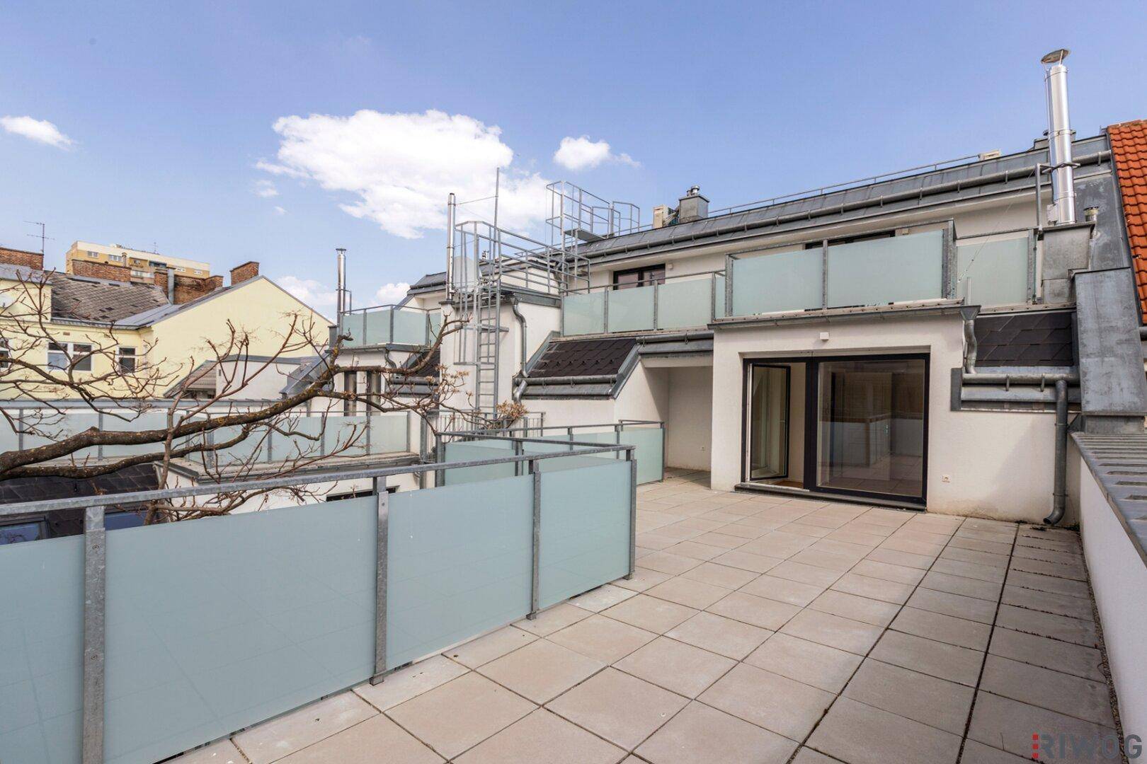 Geräumige Dachterrasse mit hellen Fliesen, modernen Glasgeländern und weitem Blick über die Stadt.