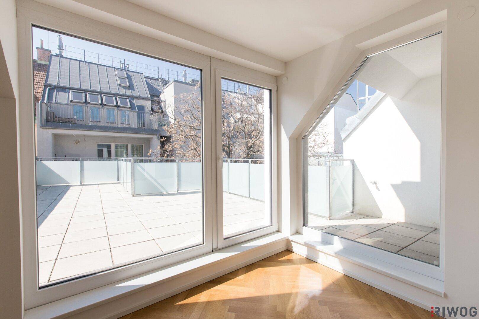 Heller Innenraum mit großen Fenstern, Parkettboden und direktem Zugang zu einer gefliesten Terrasse.