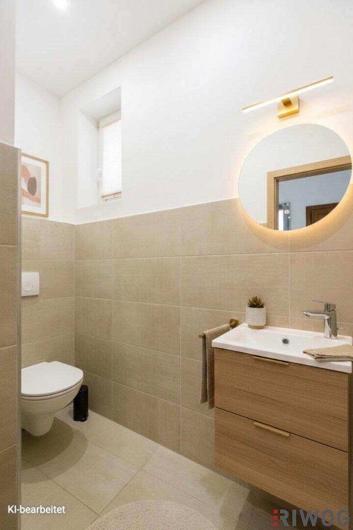 Modernes Gäste-WC mit beigefarbenen Fliesen, schwebendem Waschtisch und beleuchtetem Spiegel.
