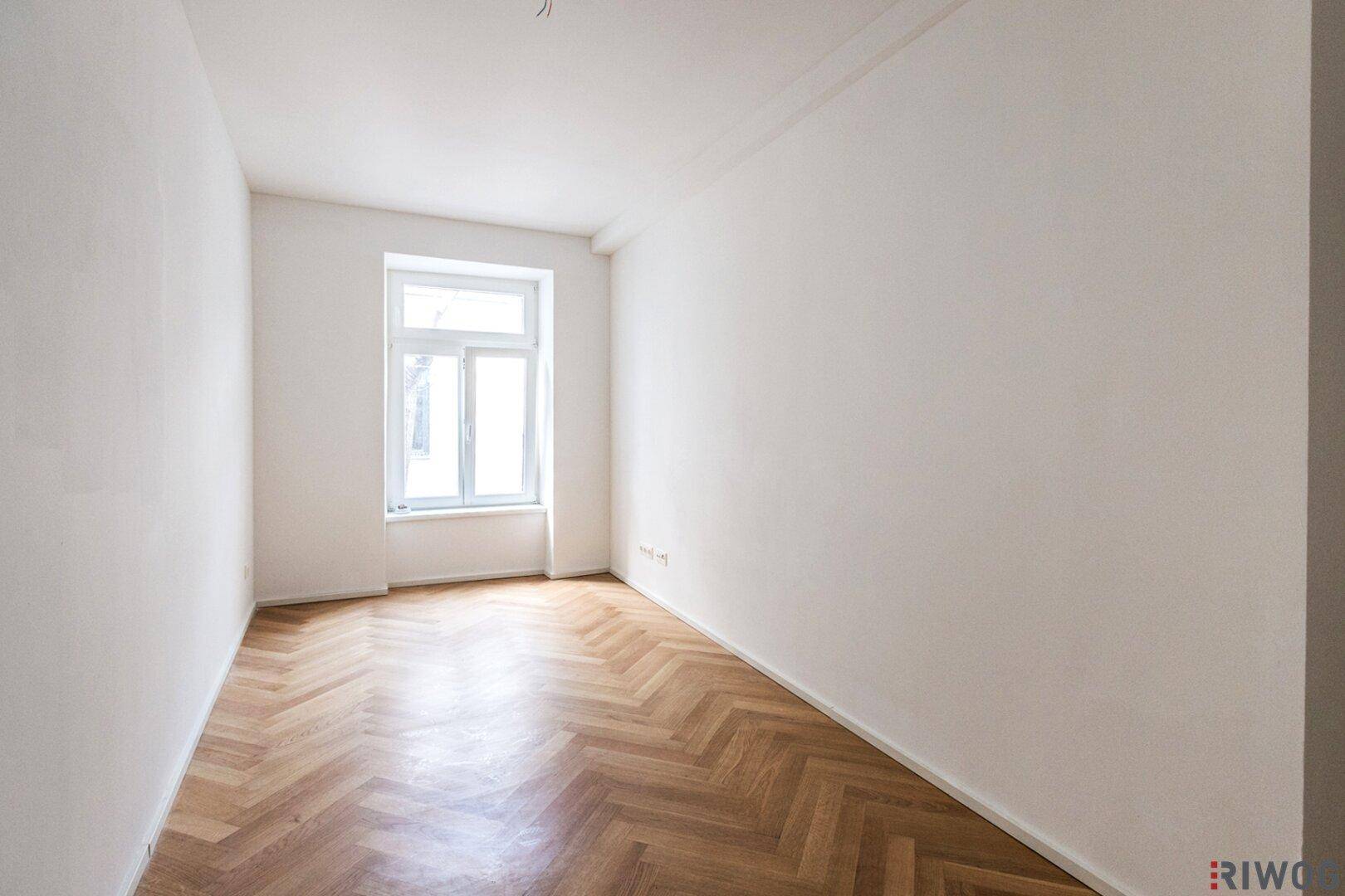 Leerer Raum mit Fischgrätparkett und einem großen Fenster, bereit zur individuellen Gestaltung.