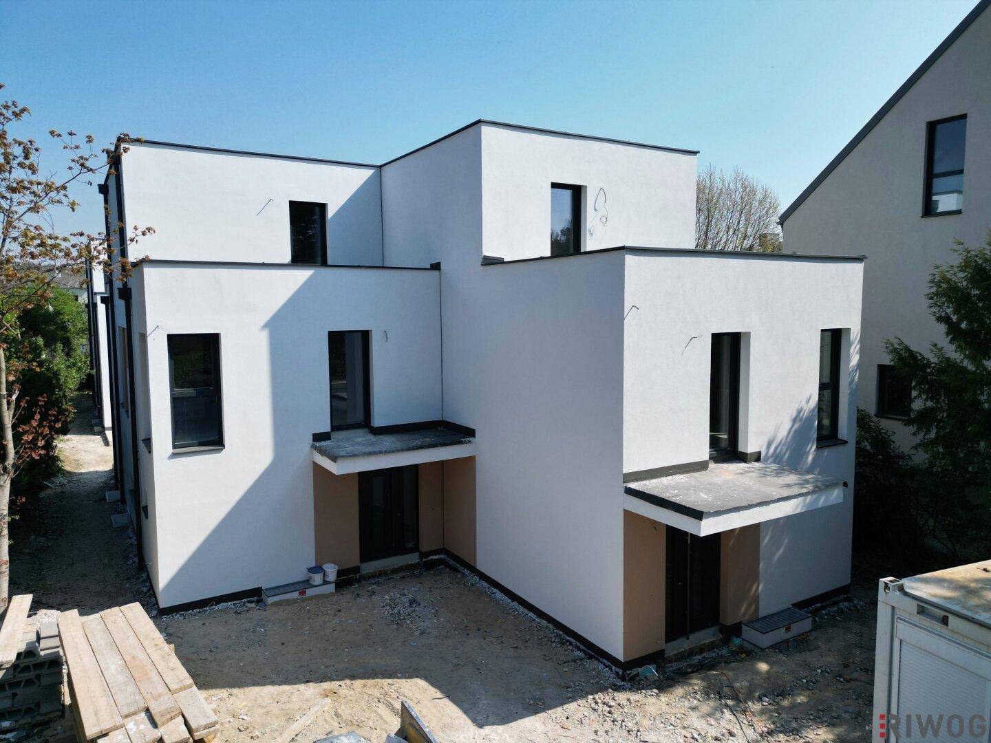 Seitenansicht eines modernen Neubaus mit weißer Fassade und großen Fensterfronten während der Bauphase.