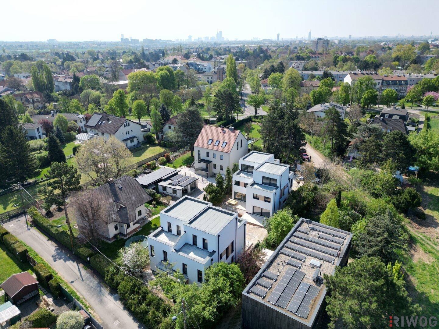 Luftaufnahme einer Wohnsiedlung mit modernen Neubauten und traditionellen Häusern unter blauem Himmel.