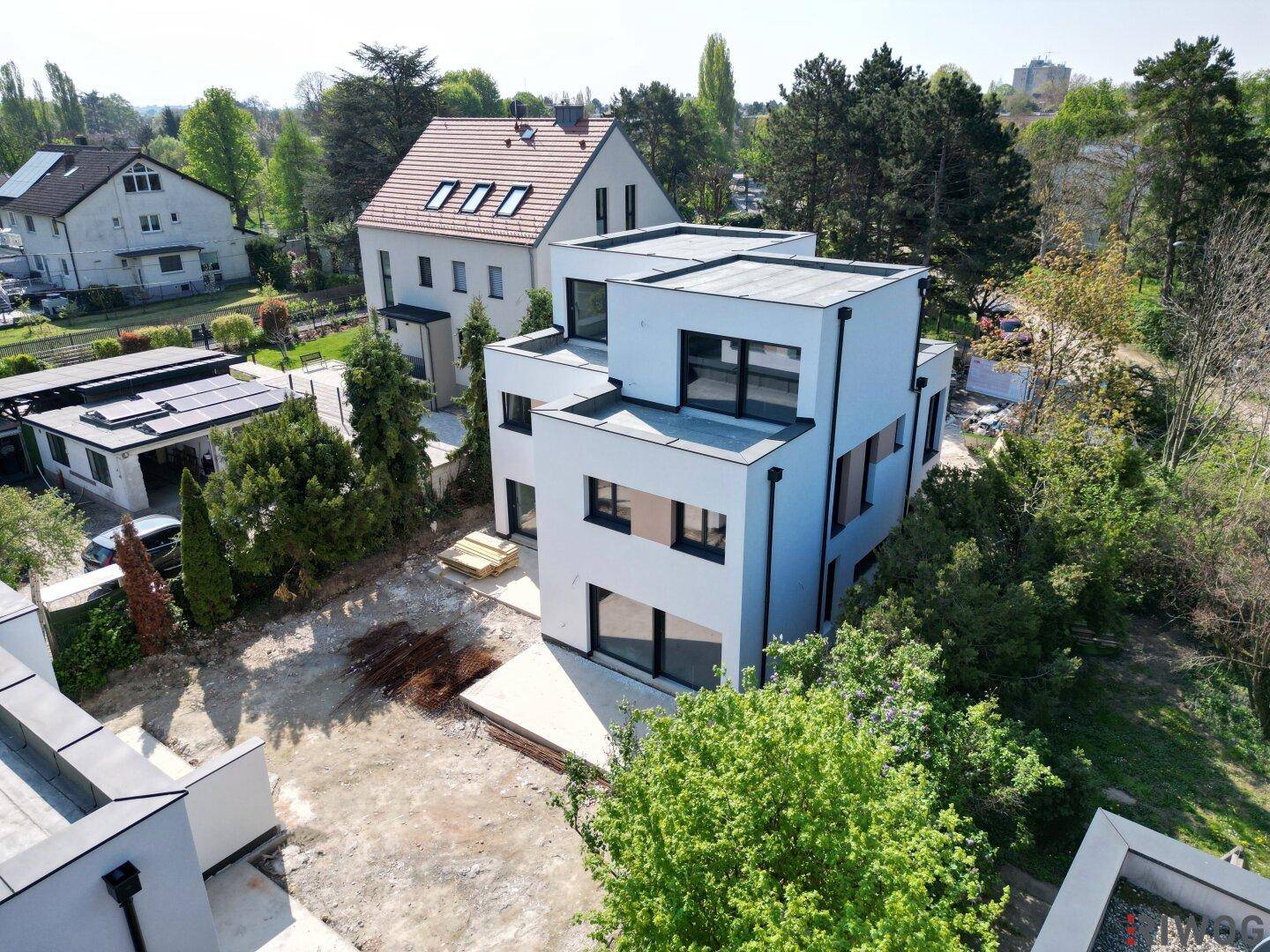 Vogelperspektive auf die moderne Architektur der weißen Neubauten mit großen Fenstern und Flachdächern in grüner Umgebung.