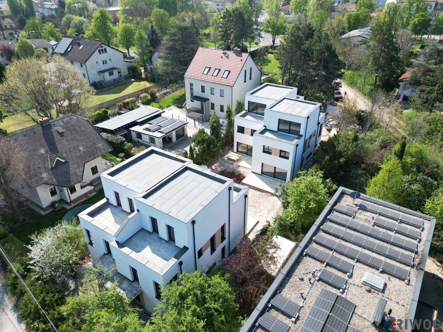 Weitläufige Luftaufnahme der modernen Neubauten eingebettet in eine grüne Wohnsiedlung mit weiteren Häusern und Solaranlagen.