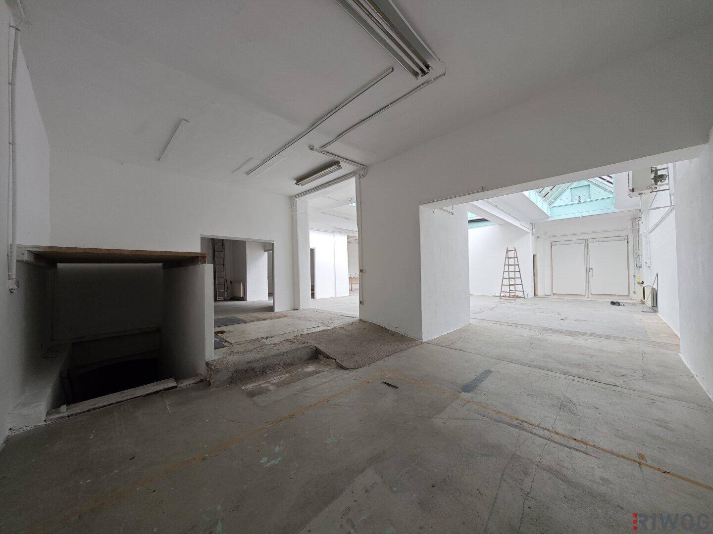 Großer Gewerberaum mit Betonboden, Leuchtstoffröhren und einer Grube im Bodenbereich.